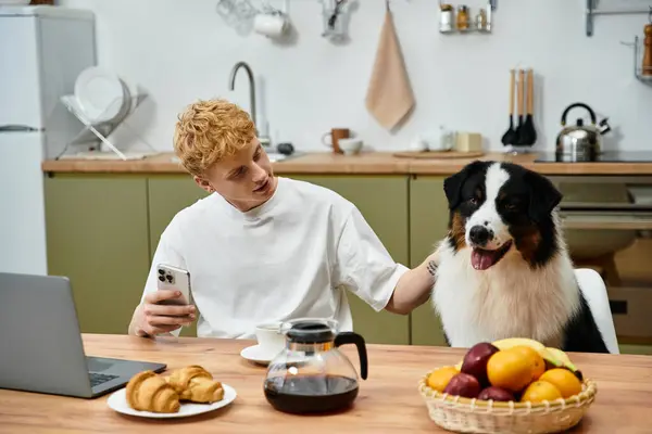 A young redhead man shares a cozy breakfast with his loyal Australian Shepherd in a modern kitchen. — Stock Photo