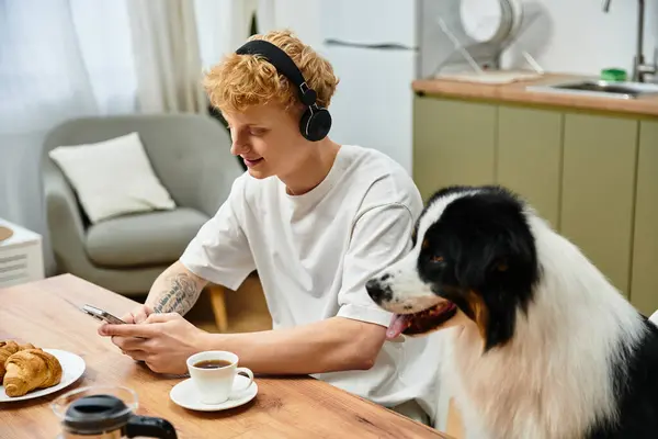 Young man with red hair relaxes at home, engaging with his dog while sipping coffee. — Stock Photo