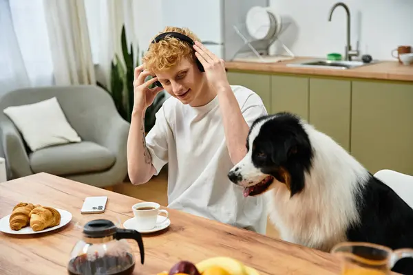 A young man with red hair shares breakfast at home with his playful Australian Shepherd dog. — Stock Photo