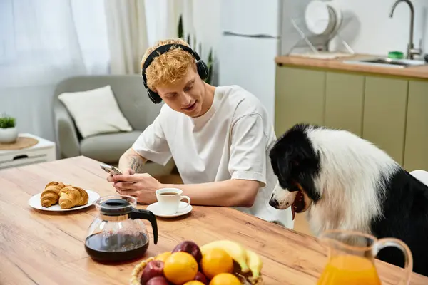 A young redhead man relaxes at home, enjoying breakfast with his Australian Shepherd dog. — Stock Photo