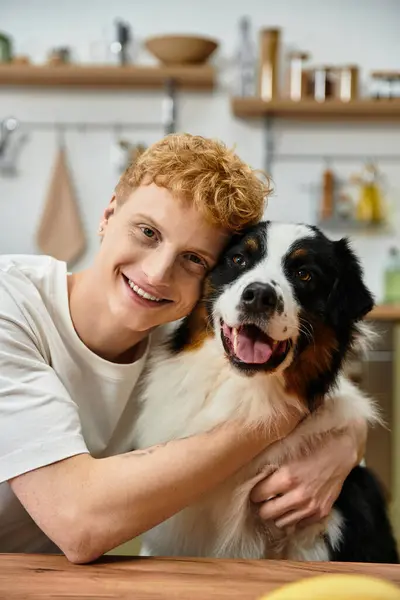 A cheerful young man with red hair hugging with his Australian Shepherd at home. — Stock Photo