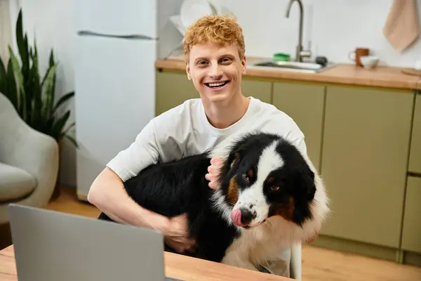 Young man laughs while cuddling his Australian Shepherd in a modern apartment setting. — Stock Photo