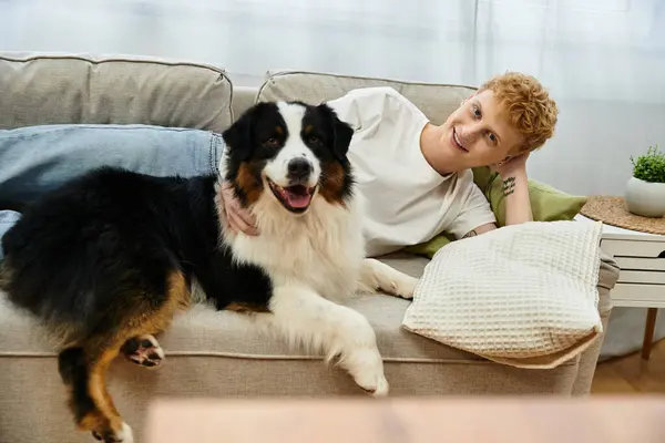 Young man relaxes on the couch with his cheerful Australian Shepherd dog in a stylish apartment. — Stock Photo