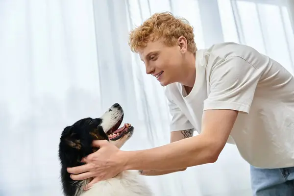 In a cozy modern apartment, a young man with red hair shares a playful moment with his dog. — Stock Photo