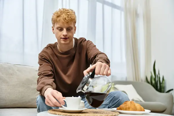 Un giovane versa il caffè in una tazza mentre è seduto a casa, assaporando una piacevole mattina. — Foto stock