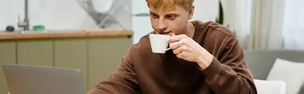 Casual dressed young redhead focuses on his laptop while enjoying a warm drink, banner — Stock Photo