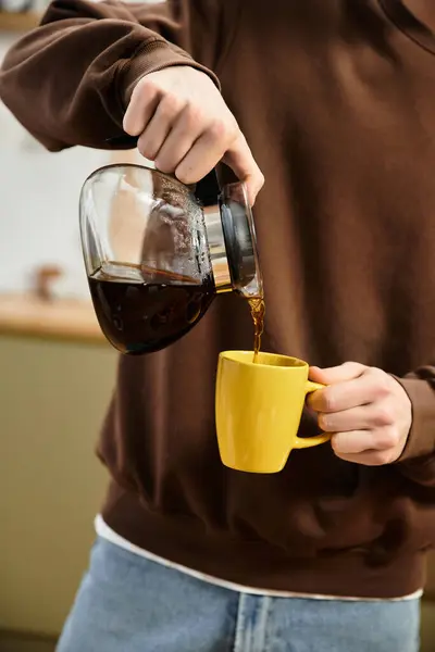 Una joven pelirroja vierte café en una taza amarilla en casa, saboreando un momento relajado. - foto de stock