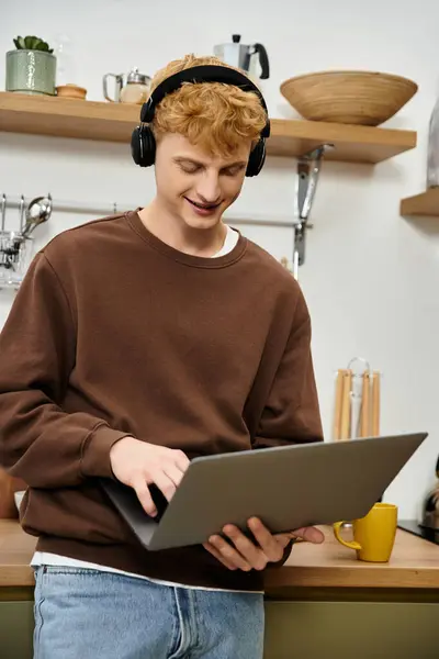 Young man with red hair engages with laptop in a contemporary kitchen setting. — Stock Photo