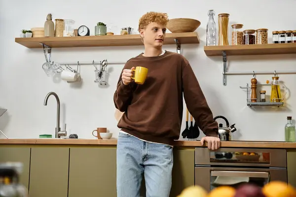 A handsome young man relaxes with coffee in a contemporary kitchen at home. — Stock Photo