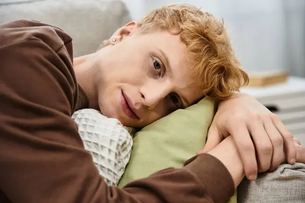 A handsome young man with red hair lounges comfortably on his couch in a chic home setting. — Stock Photo