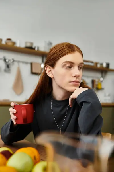 A guy with long hair sips from a red cup, relaxing in a modern and cozy apartment. — Stock Photo