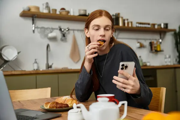 A young man relaxes in his stylish apartment, snacking and browsing his phone in the morning. — Stock Photo
