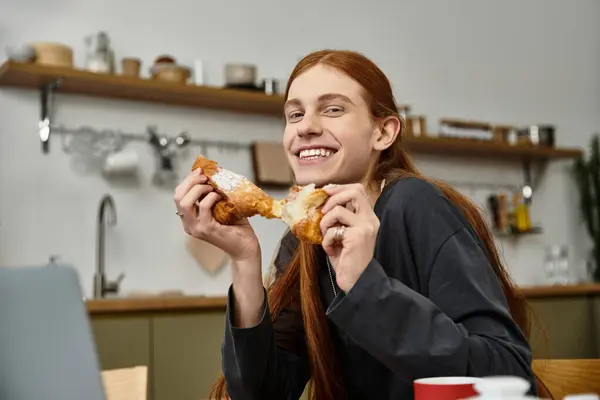 A young man with long hair smiles while enjoying a tasty meal in his cozy apartment. — Stock Photo