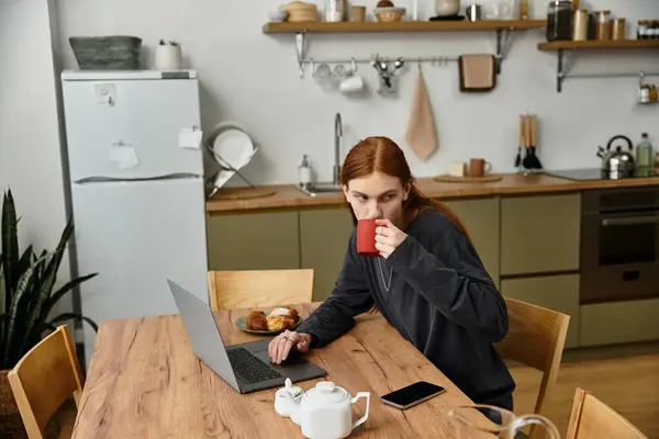 Young man in casual attire relaxes at home, sipping coffee and focusing on his laptop. — Stock Photo