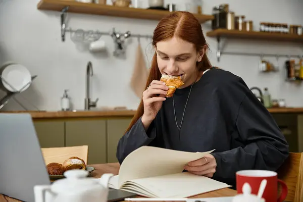 Charming young man with long hair indulges in breakfast and reading at home in the morning. — Stock Photo