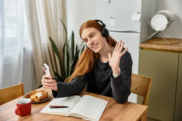 Relaxing at home, a young man chats on his phone while savoring a pastry and coffee. — Stock Photo