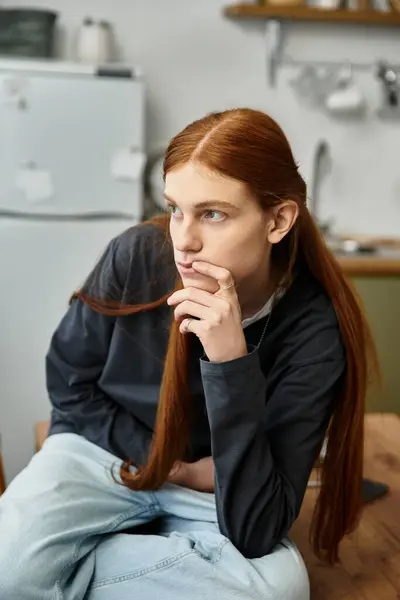 A young man with long hair ponders while sitting comfortably in his stylish apartment. — Stock Photo
