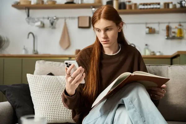 A young redheaded man relaxes in his modern apartment, enjoying a book and phone. — Stock Photo