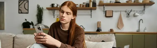 A young man sits casually in his stylish apartment, focused on his smartphone while relaxing, banner — Stock Photo