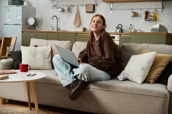 A young redhead guy in a sweatshirt enjoys a relaxing day at home, working on his laptop. — Stock Photo