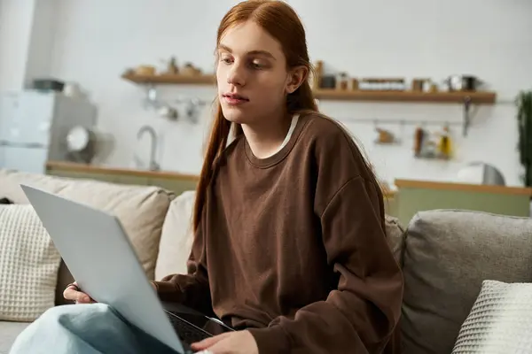 Um jovem com longos cabelos vermelhos relaxa em um apartamento moderno enquanto usa seu laptop. — Fotografia de Stock