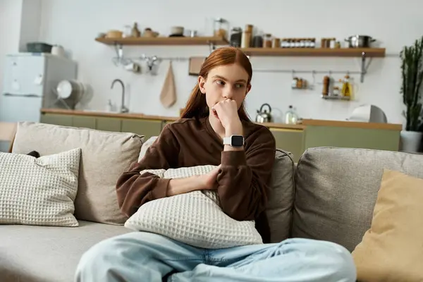 A handsome young guy with long red hair sits thoughtfully on the couch, surrounded by home comforts. — Stock Photo