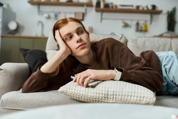 A young, handsome redhead with long hair relaxes thoughtfully on a couch. — Stock Photo