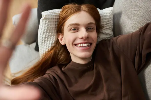 Bright smile radiates cheer as a young redhead relaxes in a stylish home setting. — Stock Photo