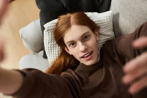 A young man with long red hair enjoys a relaxed afternoon in his stylish apartment space. — Stock Photo