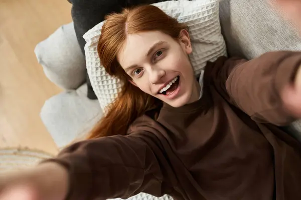 A stylish young man with long red hair relaxes on a couch, embracing a carefree lifestyle. — Stock Photo