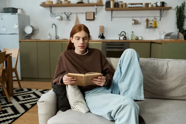 A young redhead man enjoys reading a book while lounging in a chic apartment. — Stock Photo