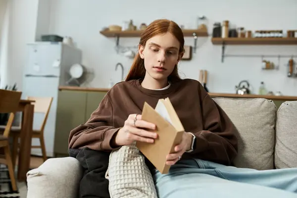 Молодой рыжий парень расслабляется дома, погружается в книгу, одеваясь непринужденно.. — стоковое фото