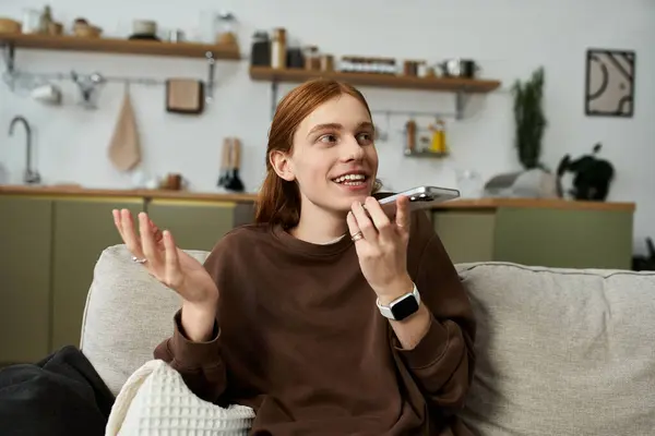 A young redhead man in a sweatshirt enjoys a lively conversation in his chic apartment. — Stock Photo