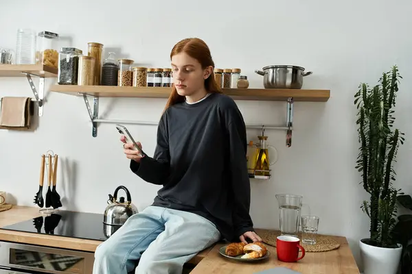 In a chic apartment, a handsome redhead relaxes on the counter while using his phone. — Stock Photo