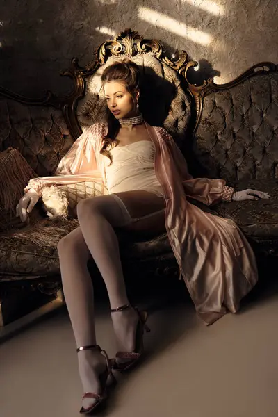 A graceful young woman relaxes on a vintage sofa, bathed in soft light and mystique. — Stock Photo