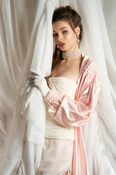 A stunning young woman in vintage attire stands gracefully behind a sheer curtain. — Stock Photo