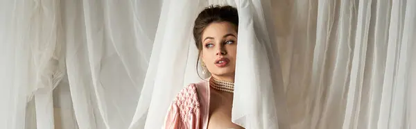 A beautiful young woman appears mystically behind sheer curtains, exuding vintage charm and allure. — Stock Photo