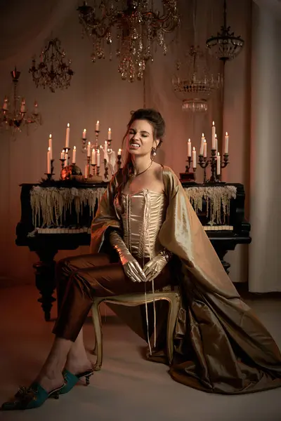 A young vampire sits elegantly in a dimly lit room with flickering candles. — Stock Photo