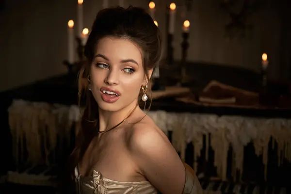 A young woman with fangs casts an enchanting gaze in a candlelit, mysterious setting. — Stock Photo