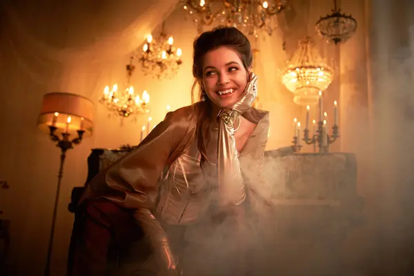 A young, beautiful vampire playfully smiles amidst a backdrop of soft candlelight and wispy fog. — Stock Photo
