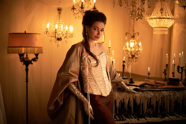 Una giovane donna abbraccia il suo personaggio vampiro in una stanza sontuosamente illuminata con lampadari. — Foto stock