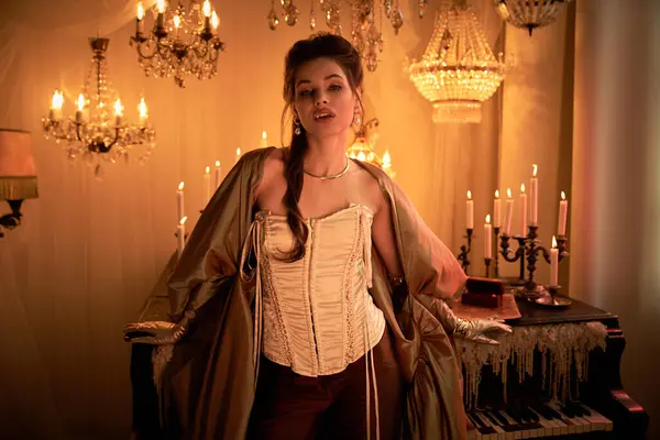 A young woman stands confidently in a dim room with chandeliers, exuding mystique. — Stock Photo