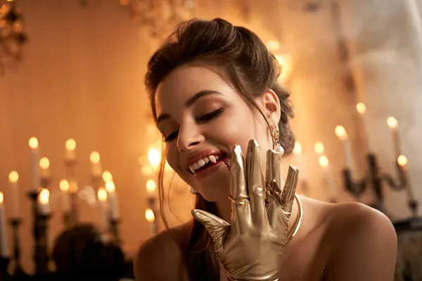 A beautiful young woman with fangs smiles playfully in candlelight, wearing a golden glove. — Stock Photo