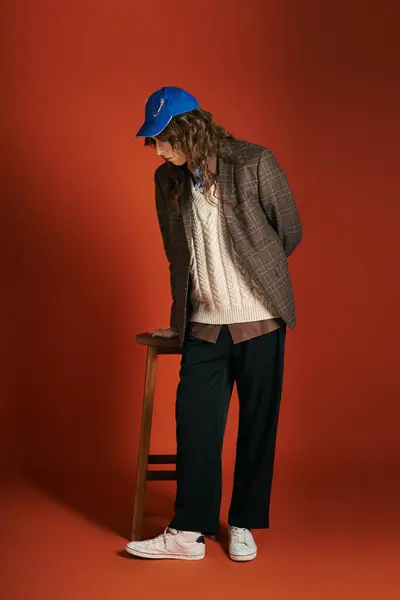 A stylish young man in trendy clothes stands pensively by a wooden stool. — Stock Photo