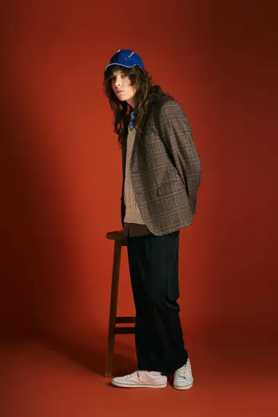 A stylish young man stands confidently beside a wooden stool, showcasing chic fashion choices. — Stock Photo