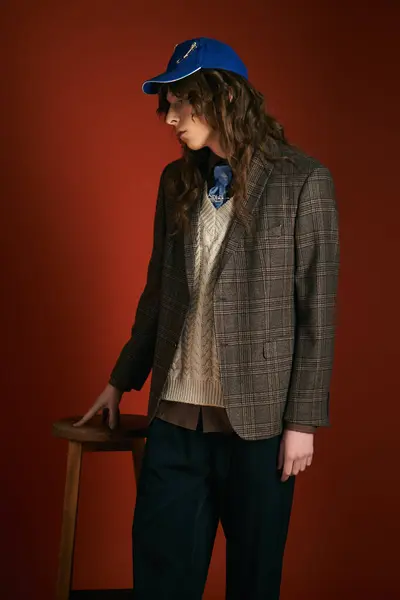 Handsome young man stands confidently near a wooden stool, exuding fashion flair in trendy outfit. — Stock Photo