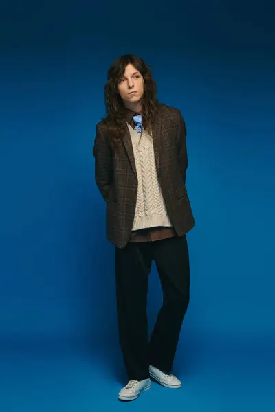 A young man confidently shows charm in a stylish outfit against a blue background. — Stock Photo