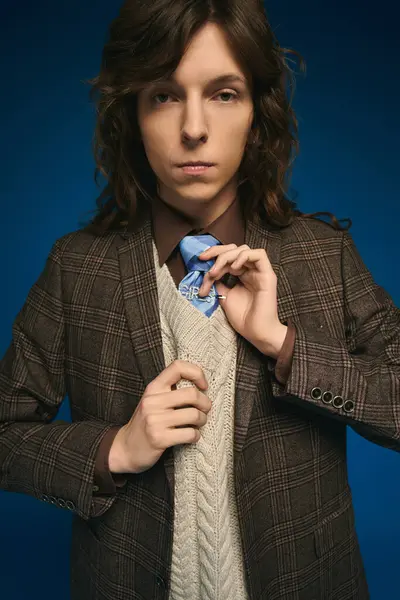 Young man adjusts his tie, displaying a chic and trendy style amidst a striking blue backdrop. — Stock Photo
