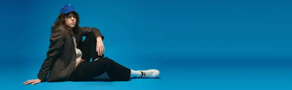A stylish young man lounges against a striking blue backdrop, showcasing modern trends. — Stock Photo