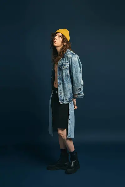 A handsome young man dressed in chic attire stands confidently against a dark backdrop. — Stock Photo